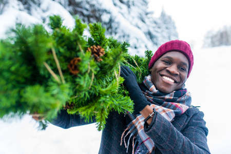 latin hispanic man in red hat , scarf and stylish coat carrying eco reusable pine tree from outdoor marketの写真素材