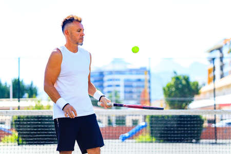 mature handsome man playing tennis on tennis court at sunny day