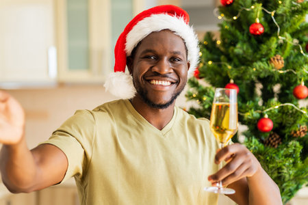 Latin hispanic man in Santa hat talking by video connection with glass of champagne at homeの写真素材