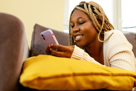 young african american woman using smartphone on couch at homeの写真素材