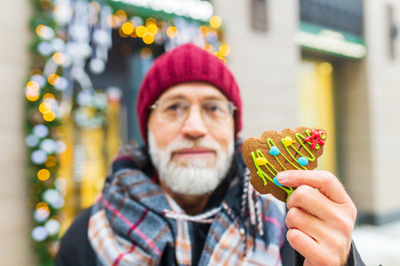 happy man showing green sweet cookie christmas tree shape outdoors in winter market