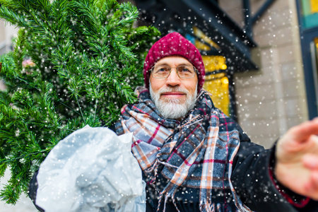happy retired man walking by street with christmas tree to home from market