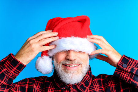 an elderly and well-groomed man in a plaid shirt and santa hat in blue studio backgroundの写真素材