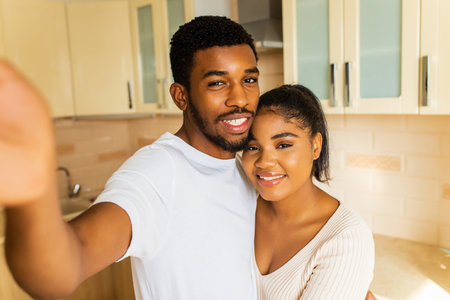 Cheerful multiethnic couple taking a selfie at the kitchenの写真素材