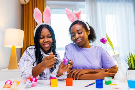 two happy sister with bunny ear painting eggs in apartment preparing to easterの写真素材