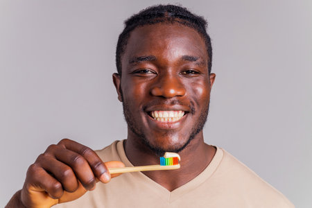 afrian american man holding colorful rainbow toothbrush in gray backgroungの写真素材