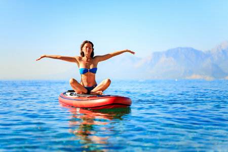 beautiful woman practising yoga on paddle sup surfboardの写真素材