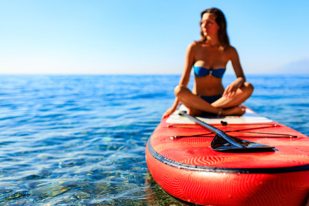 beautiful woman practising yoga on paddle sup surfboard
