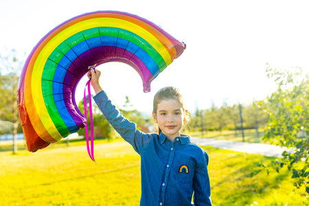 cute little brunette girl holding an air colorful rainbow balloon in summer parkの写真素材