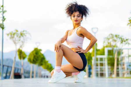 latin woman instructor with long curly hair in pink bra and black shorts posing outdoorの写真素材