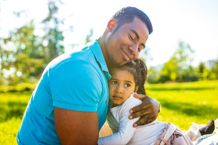 latin hispanic man with cute baby celebrating fathers day at picnic in sunny parkの写真素材