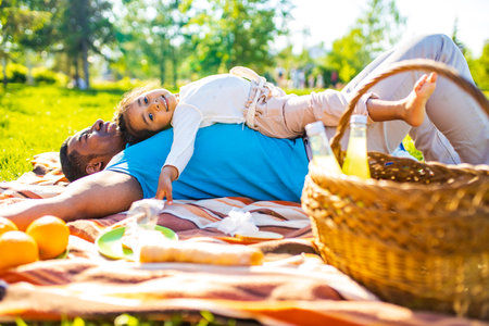 latin hispanic man with cute baby celebrating fathers day at picnic in sunny parkの写真素材