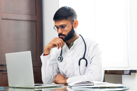 Portrait of indian man doctor talking to online patient on laptop online consultationの写真素材
