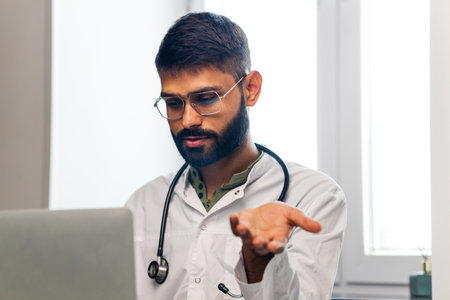Portrait of indian man doctor talking to online patient on laptop online consultationの写真素材