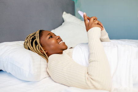 latin american woman using phone after awake in bedの写真素材