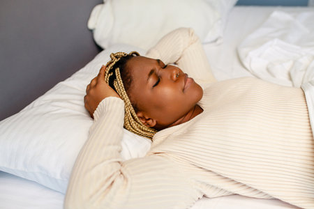 african american woman trying to sleep but headache makes it difficultの写真素材