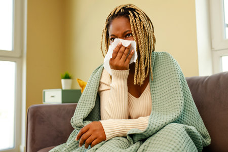 afro american woman covered with blanket blowing running noseの写真素材