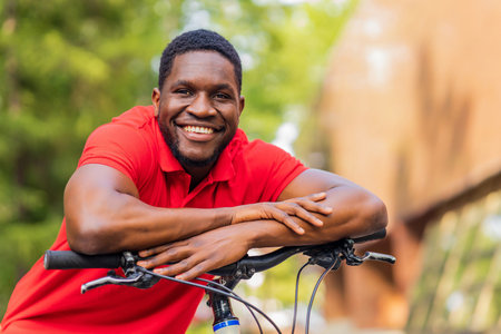 latin amerixan man in casual clothes smiling while leaning on his bikeの写真素材