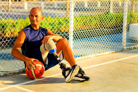 man with leg prosthesis playing basketball in tropical sea side at sumset timeの写真素材