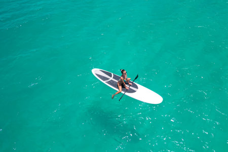 Aerial view of a woman on a white supboard in the turquoise waters of the Maldivesの写真素材