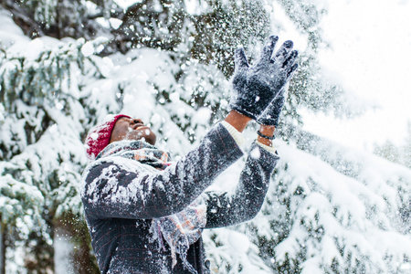 african american man in a snowy winter woodland with snowflakes falling from spruce and fir forestの写真素材