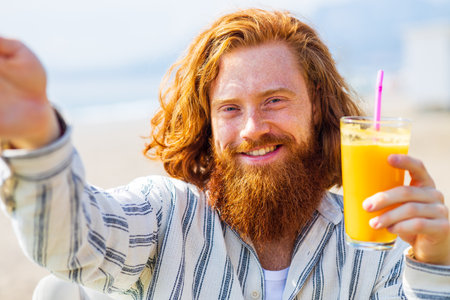young redhaired ginger bearded man working outdoors in sea cafe with laptop an summer dayの写真素材