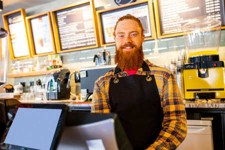 Professional barista young redhaired ginger bearded man in black apron working in coffee shopの写真素材