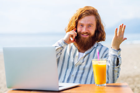 young redhaired ginger bearded man working outdoors in sea cafe with laptop an summer dayの写真素材