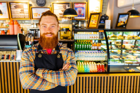 Professional barista young redhaired ginger bearded man in black apron working in coffee shopの写真素材