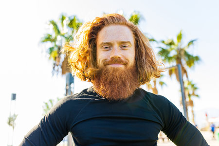 handsome redhaireb man with long beard wear black sporty suit and warming up in sunny beachの写真素材