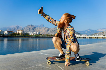 handsome redhaired man with long beard skateboarding near river at sunny summer dayの写真素材