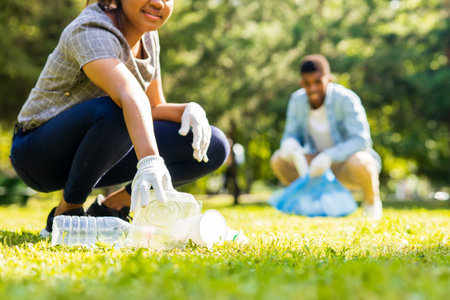 afro american volunteers collecting plastic trash at sunny day in summer parkの写真素材