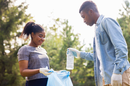 afro american volunteers collecting plastic trash at sunny day in summer parkの写真素材