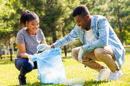 afro american volunteers collecting plastic trash at sunny day in summer parkの写真素材