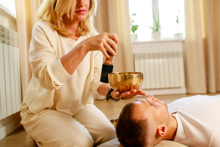 Woman playing on a tibetian singing bowl maling massage meditation for a manの写真素材
