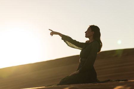 woman in green long dress stands in desert sand dunes background yellow orange sunsetの写真素材