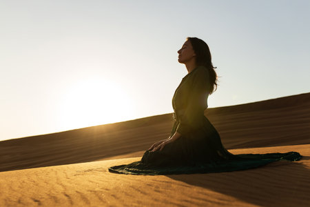 woman in green long dress stands in desert sand dunes background yellow orange sunsetの写真素材