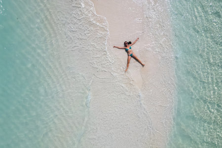 young woman tanning sunbathing woman wearing bikini at the beach on a white sand from above view...