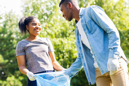 afro american volunteers collecting plastic trash at sunny day in summer parkの写真素材