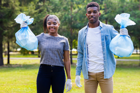 afro american volunteers collecting plastic trash at sunny day in summer parkの写真素材