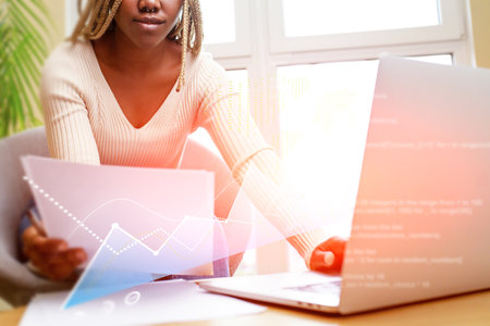 A woman is sitting at a desk with a laptop and a stack of papersの写真素材