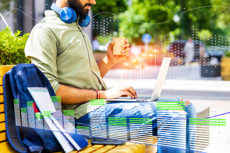 A man is sitting on a bench with a laptop and a cup of coffeeの写真素材
