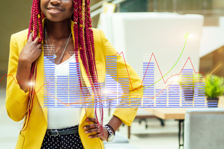 A woman in a yellow jacket stands in front of a graph with a smile on her faceの写真素材