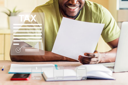 A man is sitting at a desk with a laptop and a stack of papersの写真素材