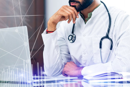 A doctor is sitting at a desk with a laptop and a stethoscopeの写真素材