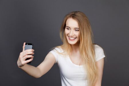 young pretty blonde women taking selfie on cell phone in studioの写真素材