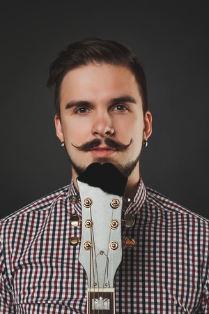 handsome guy with beard and mustache with acoustic guitar on dark backgroundの写真素材