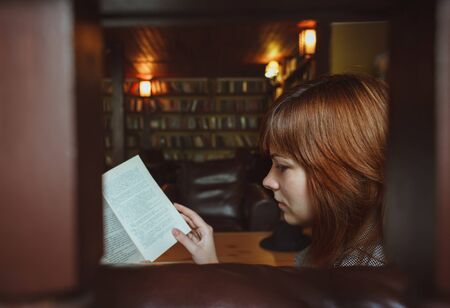 Beautiful female student in a university library reading bookの写真素材