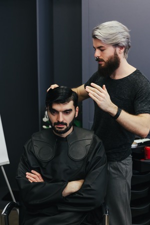 Male barber combing and shaving hair of a male client at barbershopの写真素材