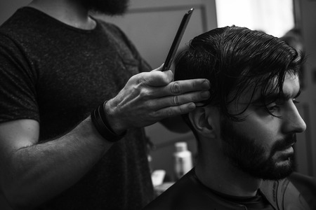 Male barber combing and shaving hair of a male client at barbershopの写真素材